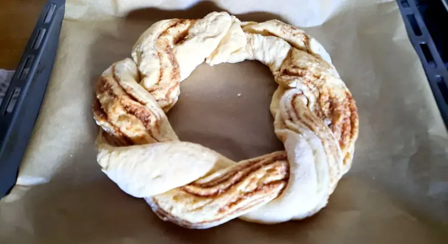 Ein geflochtener Teigring mit Zimtfüllung liegt auf Backpapier. Perfekt für das Osterkranz backen.
