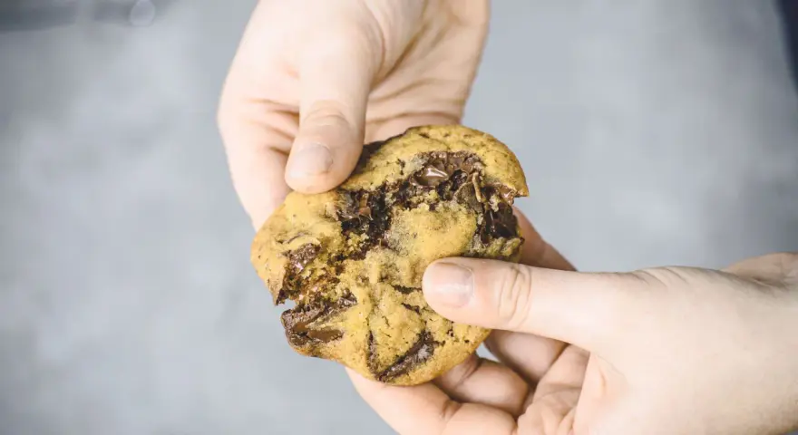 Hände halten einen zerkrümelten Schokoladenkeks, der nach einem einfachen Cookies Rezept gemacht wurde.