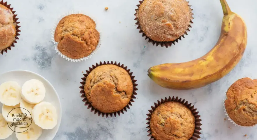 Leckere Bananen Muffins, frisch gebacken, mit einer reifen Banane und Bananenscheiben daneben.