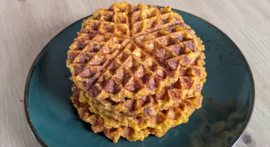 Ein Stapel goldbrauner Haferflocken Waffeln auf einem dunklen Teller. Sie sehen knusprig und lecker aus, perfekt für ein gesundes Frühstück.