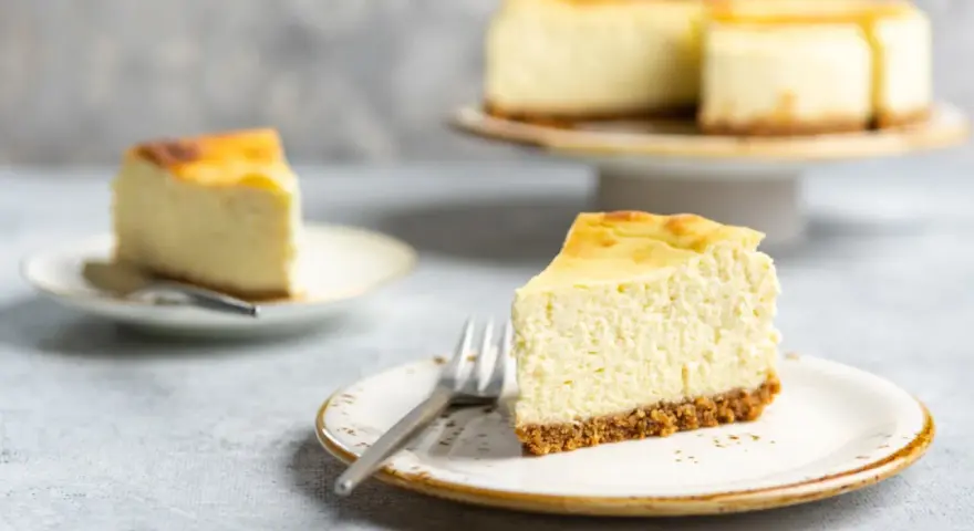 Ein cremiger Kuchen mit Mascarpone, auf einem Teller mit Gabel, daneben ein weiteres Stück und ein ganzer Kuchen.