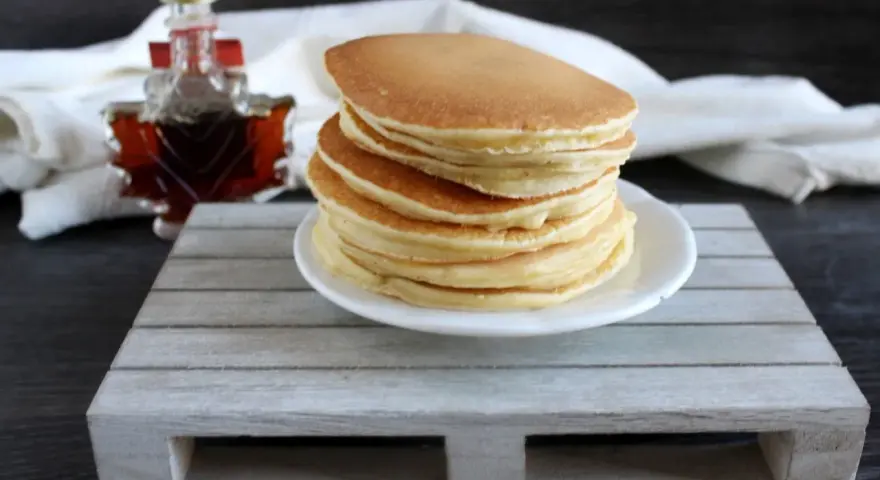Ein Stapel goldbrauner Pfannkuchen, bereit für ein köstliches Frühstück. Daneben eine kleine Flasche Ahornsirup. Ein einfaches Pfannkuchen Rezept für jeden Tag.