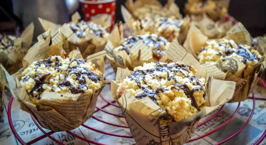 Saftige Nutella Muffins mit Streuseln und Schokoglasur, verpackt in Zeitungspapier-Förmchen, auf einem roten Gitter.