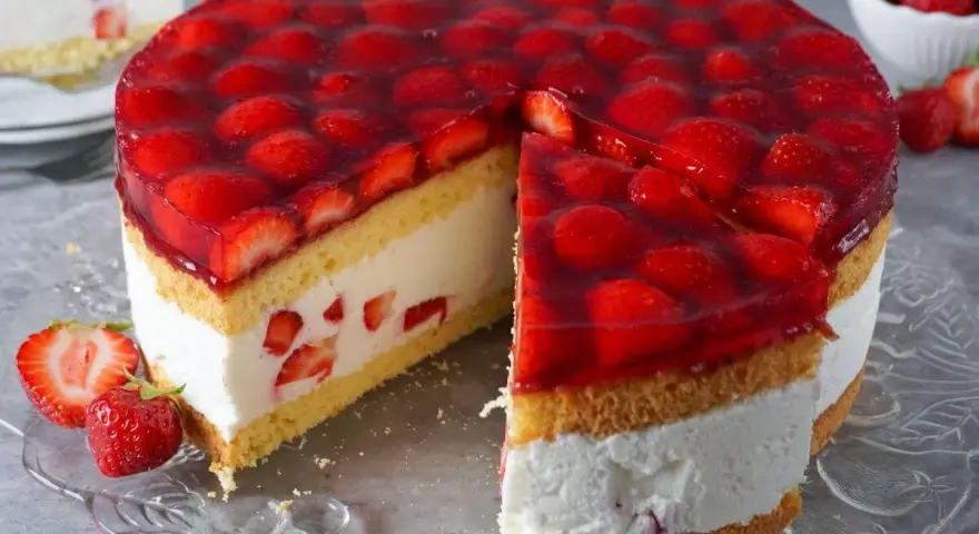 Eine saftige Erdbeer Sahne Torte mit frischen Erdbeeren und Tortenguss, ein Stück ist bereits angeschnitten.