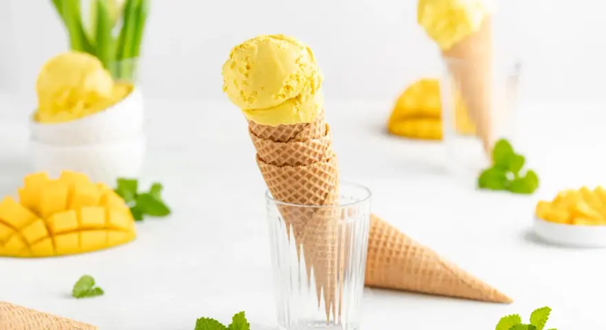 Ein Stapel Waffelkegel mit cremigem Mango Eis, garniert mit frischer Minze und Mangostücken. Ein süßer Genuss!
