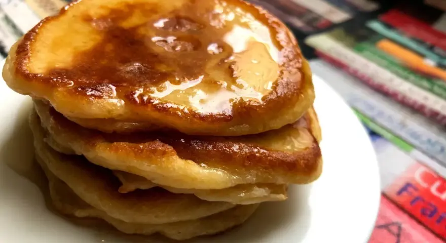 Ein Stapel goldbrauner Pancakes mit Kefir, beträufelt mit Honig, auf einem weißen Teller.
