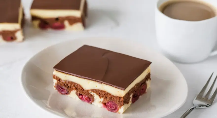 Ein Stück Donauwelle-Kuchen mit Kirschen, Vanillecreme und Schokoladenglasur. Ein leckeres Rezept für den Kaffeetisch.