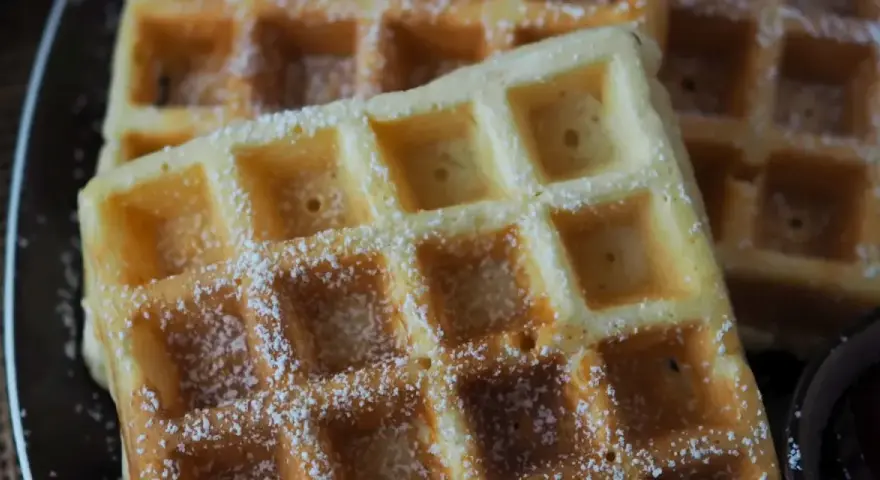 Goldbraune Waffeln, bestäubt mit Puderzucker, warten auf Joghurt. Ein süßer Genuss!