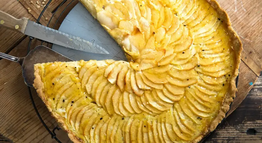 Ein köstliches Apfeltarte Rezept mit dünn geschnittenen Äpfeln, die wie Fächer angeordnet sind. Ein Stück wurde bereits herausgeschnitten.