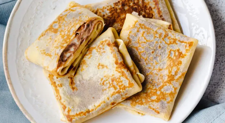 Gefaltete Crêpes mit Schokoladencreme-Füllung, ein köstliches Crepes Rezept, liegen auf einem Teller.