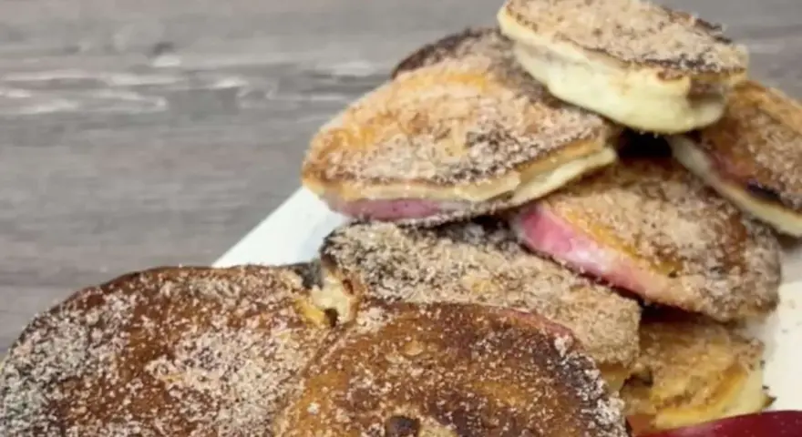 Ein Haufen goldbrauner, mit Zimt und Zucker bestreuter Apfelküchlein, die köstlich aussehen.