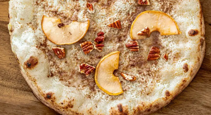 Eine süße Pizza mit dünnem Teig, bestreut mit Zimt, belegt mit Apfelscheiben und Pekannüssen. Ein Genuss wie eine Nutella Pizza!
