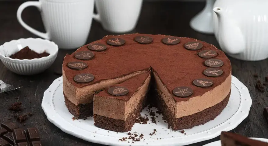 Eine köstliche Schoko Torte, bestäubt mit Kakao und verziert mit Schokoladensternen und -hirschen. Ein Stück ist bereits angeschnitten.