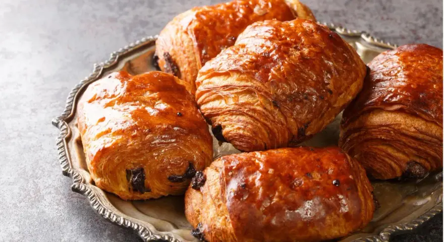 Einige goldbraune, knusprige Pain au Chocolat liegen auf einer silbernen Platte.