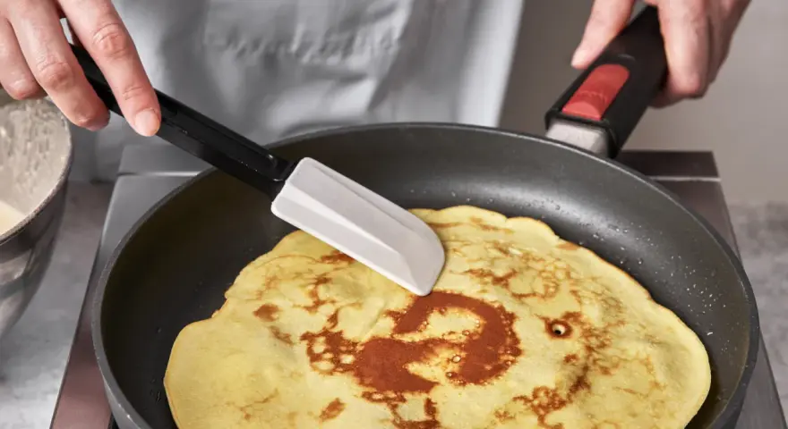 Ein goldbrauner Quark Pfannkuchen wird in einer Pfanne mit einem Spatel gewendet.