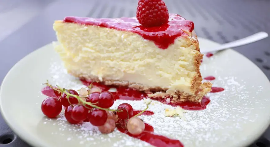 Ein Stück cremiger Käsekuchen mit Himbeersoße und frischen Beeren, bestäubt mit Puderzucker. Ein Genuss für alle Sinne, diese Himbeer Torte.