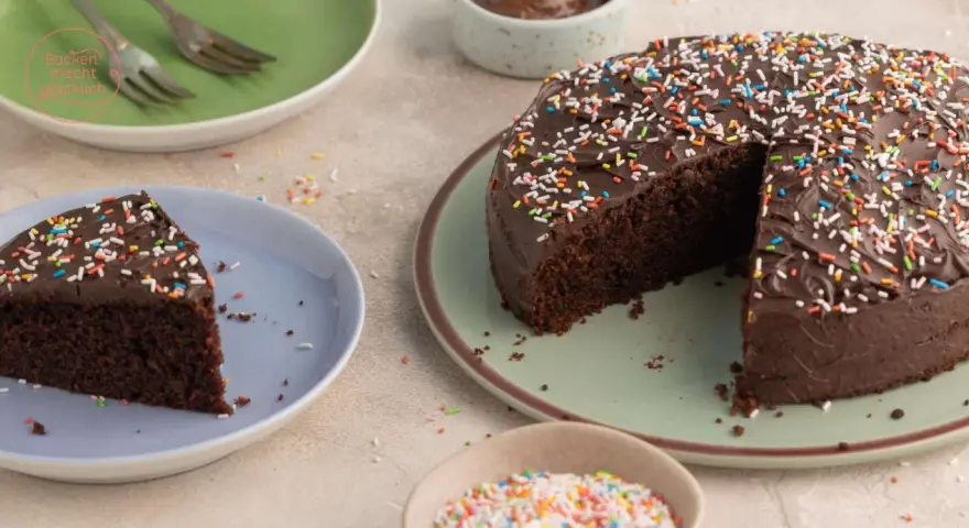 Ein saftiger Nutella Kuchen mit Schokoladenglasur und bunten Streuseln, ein Stück auf einem Teller, bereit zum Genießen.