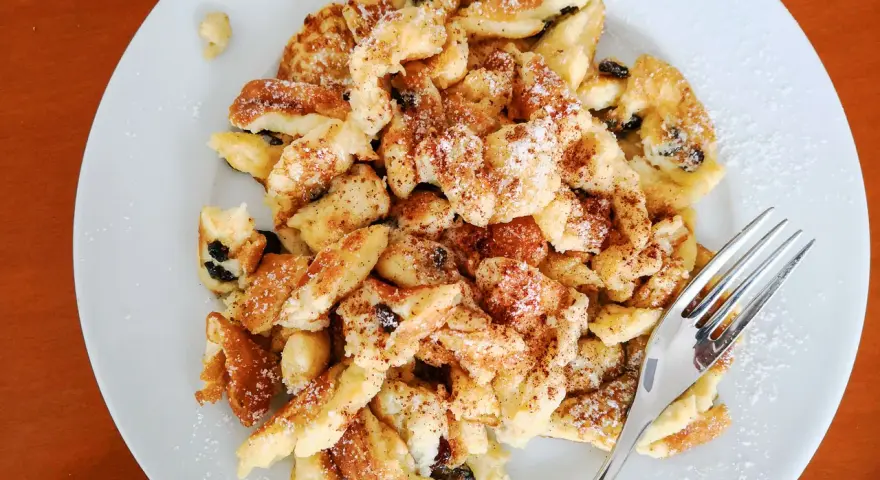 Ein Teller Kaiserschmarrn, bestreut mit Puderzucker und Zimt, wartet auf seine Verkostung. Dieses Kaiserschmarrn Rezept ist ein Klassiker.