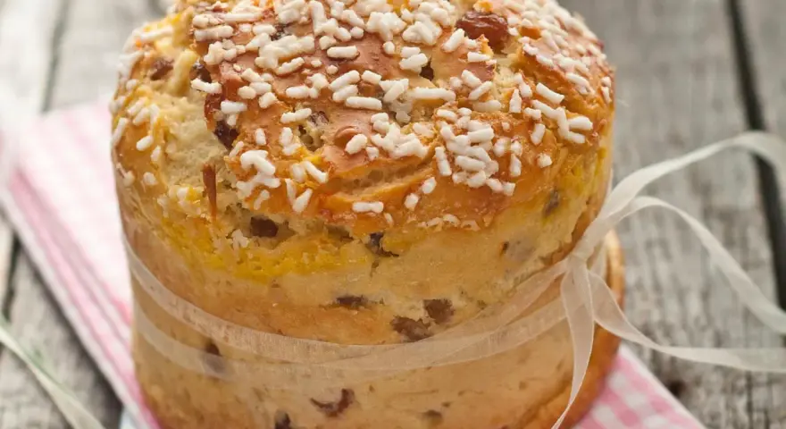 Ein goldbrauner Panettone mit Rosinen und Zuckerkristallen, gebunden mit einem Satinband. Ein köstliches Panettone Rezept zum Nachbacken.