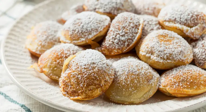 Ein Teller voller goldbrauner Poffertjes, bestäubt mit Puderzucker. Dieses Poffertjes Rezept ist ein Genuss!