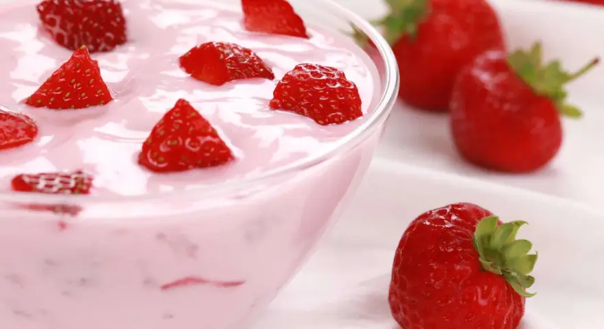 Ein cremiges Erdbeer Dessert in einer Schüssel, garniert mit frischen Erdbeerstücken. Daneben liegen ganze Erdbeeren.
