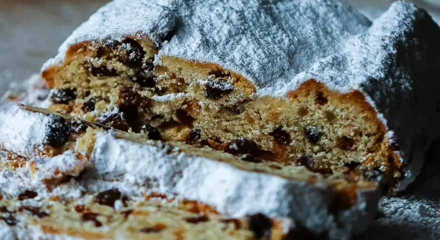 Ein saftiger Stollen, bestäubt mit Puderzucker, zeigt sein Inneres voller Rosinen. Ein köstliches Stollen Rezept zum Nachbacken.