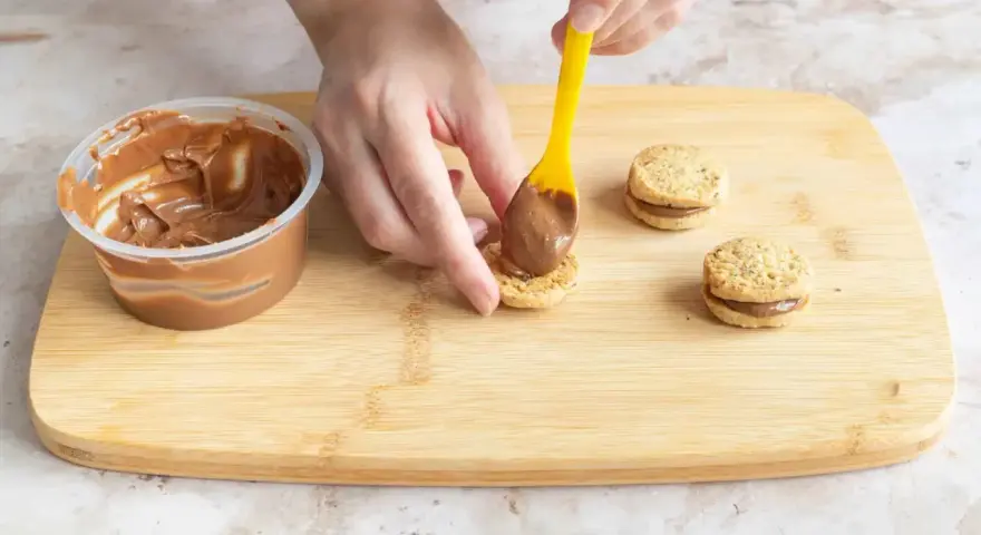 Hände belegen Kekse mit Nutella. Leckere Nutella Kekse entstehen auf dem Holzbrett.