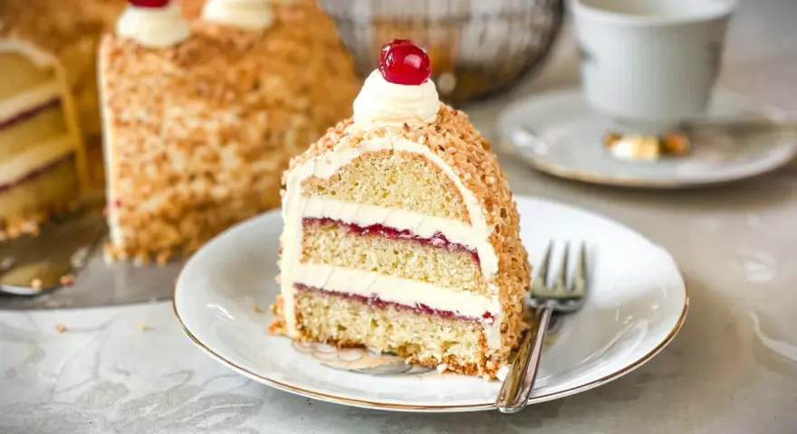 Ein Stück Frankfurter Kranz mit Buttercreme und Kirschen, umhüllt von gehackten Nüssen. Ein Genuss für jeden Kaffeetisch.