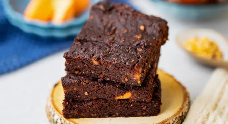 Gestapelte, saftige vegane Brownies mit Nüssen, auf einem Holzscheit.