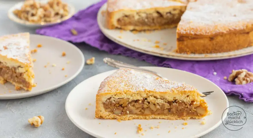 Ein Stück Nusstorte mit Puderzucker bestreut, perfekt für ein leckeres nusstorte rezept. Walnüsse liegen daneben.