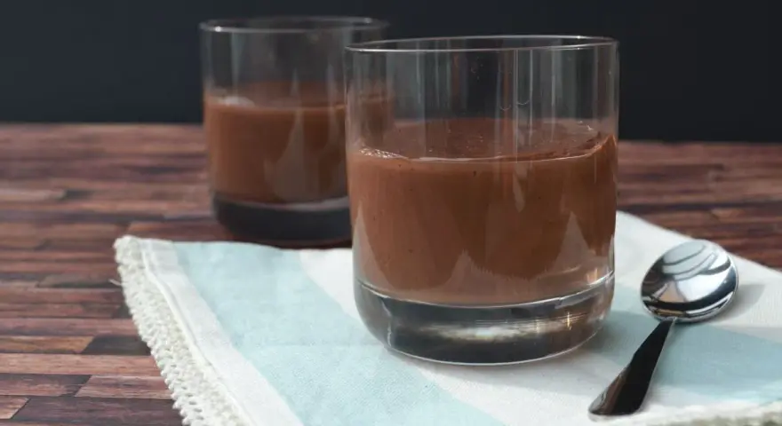 Zwei Gläser cremiger Schokopudding, perfekt zum Schokopudding selber machen. Ein Löffel liegt bereit.