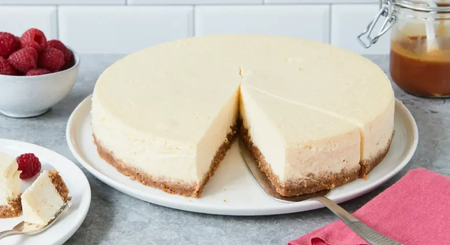 Ein cremiger New York Cheesecake mit knusprigem Boden, garniert mit Himbeeren und Karamell.