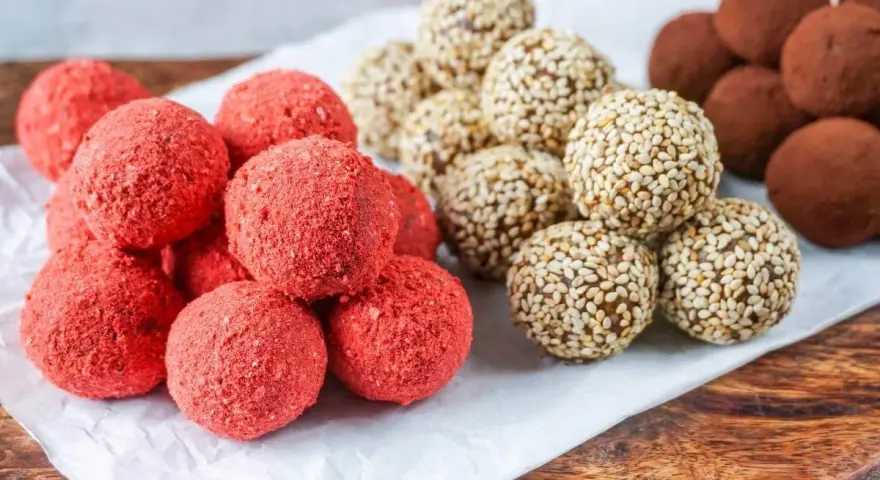 Drei Sorten leckere Energy Balls: rote Erdbeer-Bällchen, mit Sesam umhüllte Kugeln und schokoladige Trüffel.