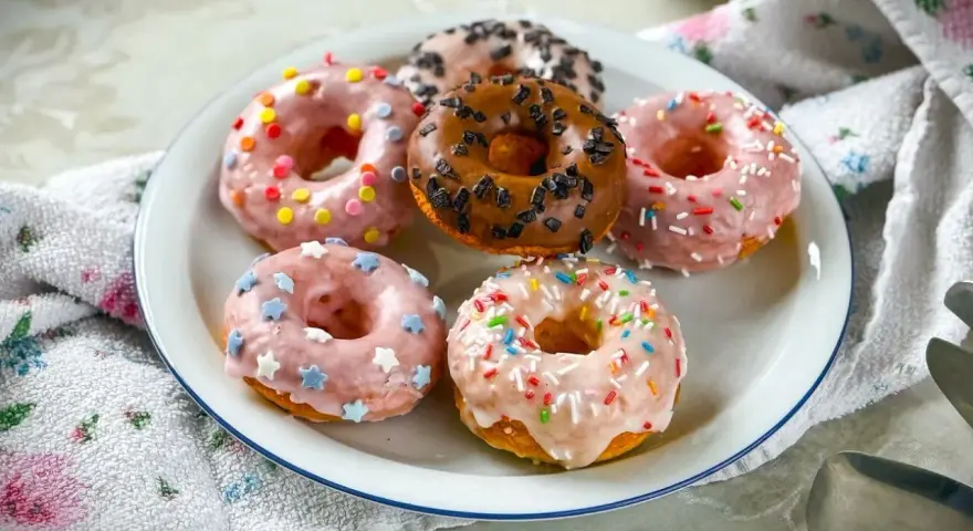 Sechs bunte Donuts auf einem Teller, perfekt für ein schnelles Donuts Rezept. Mit Streuseln und Sternen verziert.