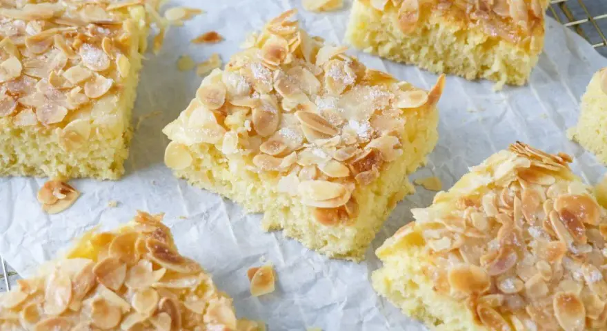 Saftiger Buttermilchkuchen mit Mandeln, bestreut mit Zucker, auf Backpapier und einem Gitter.