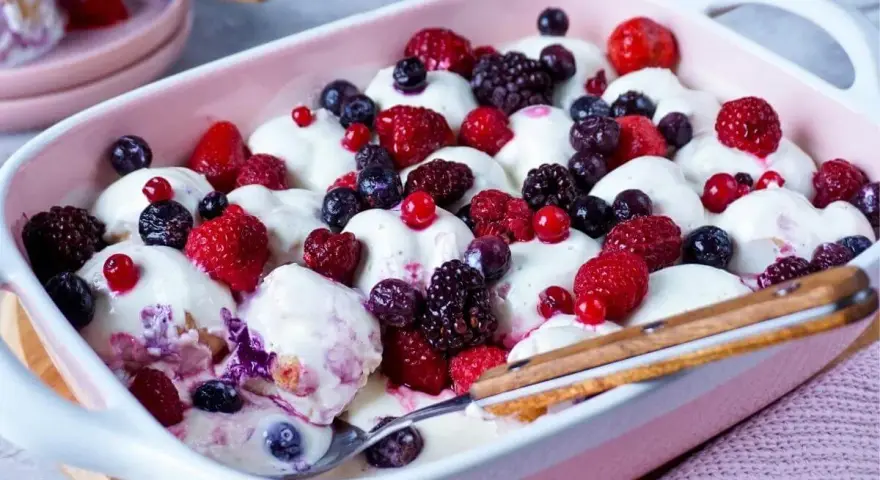 Ein cremiges Windbeutel-Dessert mit frischen Beeren wie Himbeeren, Brombeeren und Blaubeeren, serviert in einer rosa Schale.