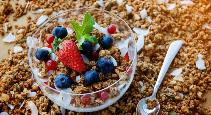 Schüssel mit frischem Granola, Beeren und Kokosflocken. Perfekt für ein gesundes Frühstück, wenn du Granola selber machen möchtest.