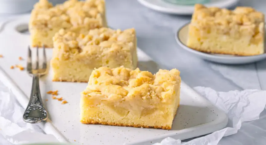 Saftiger Apfelkuchen mit Streuseln, perfekt für eine Kaffeepause. Ein Stück ist schon auf einer kleinen Platte angerichtet.