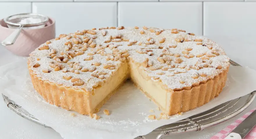 Eine köstliche Torta della Nonna, bestäubt mit Puderzucker und Pinienkernen, wartet darauf, angeschnitten zu werden.