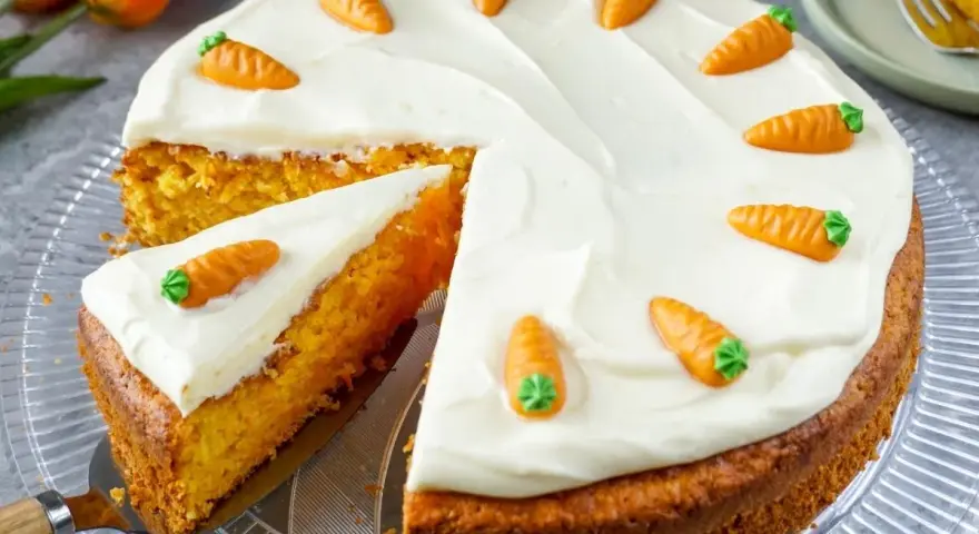 Saftiger Karottenkuchen mit cremigem Frosting und süßen Marzipan-Karotten. Ein Stück ist bereits angeschnitten.