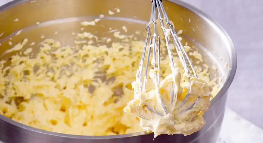 Ein Schneebesen mit cremigem Teig, bereit für ein Buttercreme Rezept.