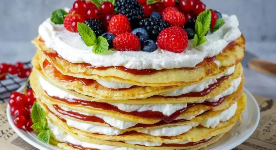 Eine hohe Pfannkuchen Torte mit Sahne und roter Marmelade, gekrönt mit frischen Beeren und Minze.