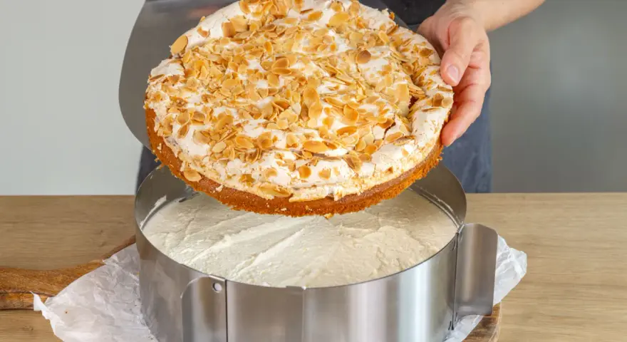 Eine köstliche Stachelbeer Baiser Torte mit Mandel-Topping wird gerade in einen Tortenring gesetzt.