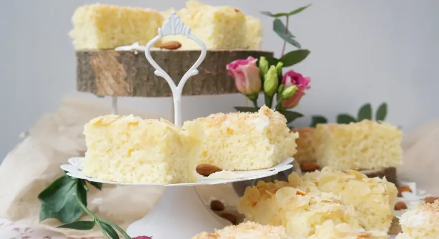 Saftige Buttermilchkuchenstücke mit Mandelsplittern und Kokosraspeln, garniert mit Blumen.