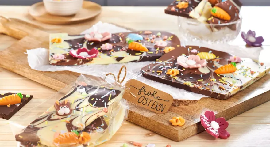Bruchschokolade selber machen: Bunte Oster-Schokoladentafeln mit Karotten, Blumen und Streuseln, verpackt und mit "Frohe Ostern"-Anhänger.