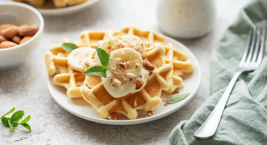 Goldbraune Skyr Waffeln mit Bananenscheiben, gehackten Mandeln und Minze. Ein köstlicher Start in den Tag!