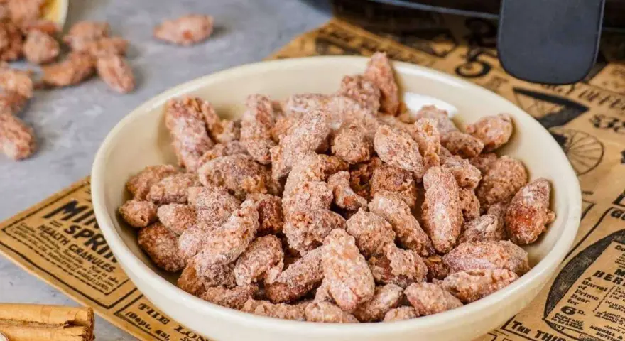 Schüssel voller gebrannter Mandeln, perfekt für ein schnelles gebrannte mandeln rezept. Zimtstangen liegen daneben.