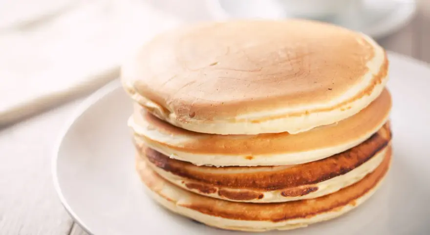 Ein Stapel goldbrauner, glutenfreier Pfannkuchen auf einem weißen Teller, bereit zum Genießen.