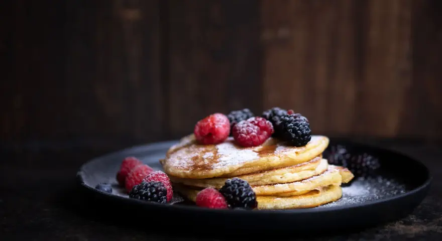 Stapel goldbrauner Pancakes, bestäubt mit Puderzucker und garniert mit frischen Himbeeren und Brombeeren. Ein köstliches Pancakes Rezept für jeden Anlass.