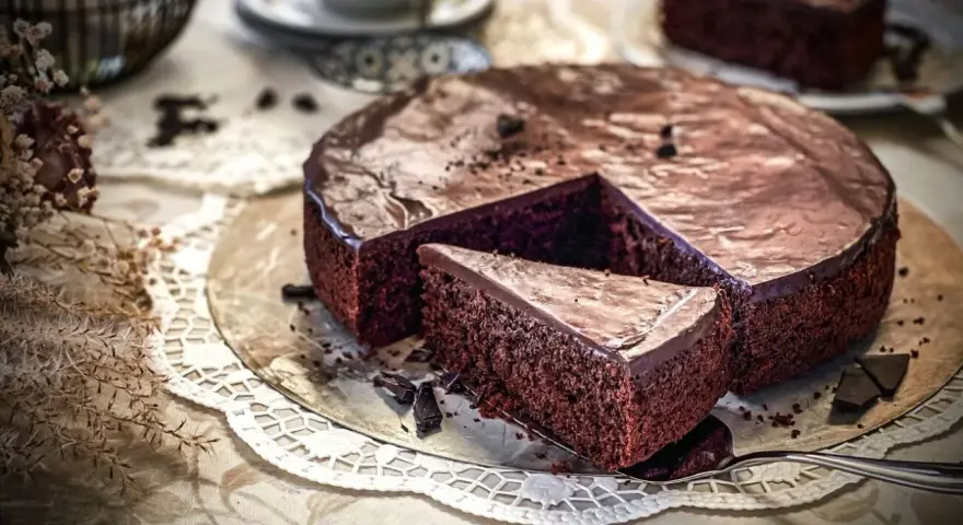 Ein saftiger, schneller Schokokuchen mit glänzender Glasur und einer Kuchenscheibe auf einem Tortenheber.